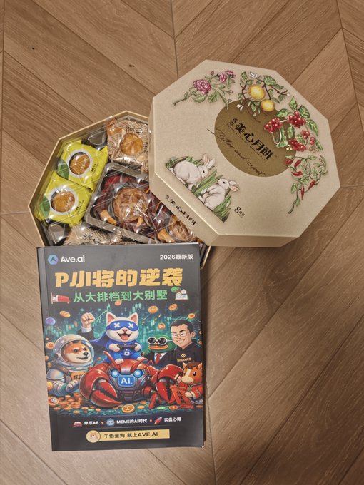 A promotional display on a wooden floor shows an open octagonal gift box of assorted cookies next to a magazine featuring a Shiba Inu astronaut, a Shiba Inu robot, and the text 'Ave.ai', '2026 最新版', and 'PJ 将的逆袭'.