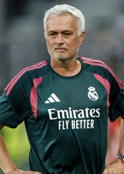 A man with gray hair wears a dark green Real Madrid training jersey featuring the 'Emirates FLY BETTER' sponsor logo and pink shoulder accents.