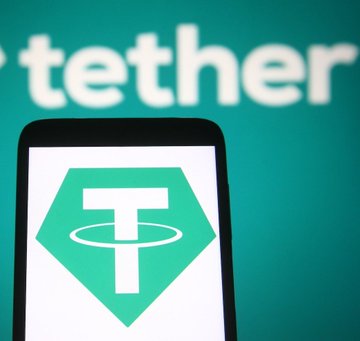 The image shows a smartphone displaying the Tether "T" logo against a green background with the word "tether" visible behind the phone, visually reinforcing the post's announcement that Tether has received a clean financial audit from KPMG confirming $6.8 billion in excess reserves over liabilities.