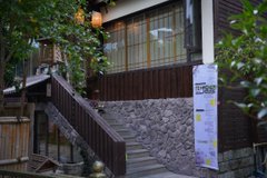 A small, slightly blurry image showing a building with a tiled wall, stairs, and a white sign, partially framed by green leaves.