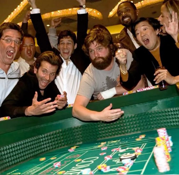 A group of excited men cheering at a craps table in a casino, with casino chips scattered on the green felt table.