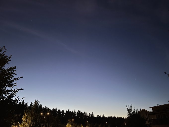 A twilight sky over a silhouetted treeline with two faint celestial objects (likely a comet and a planet) visible above the horizon.