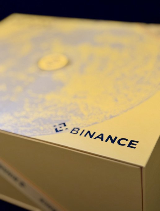 A close-up of a yellow Binance branded box with a world map design and the Binance logo clearly visible.