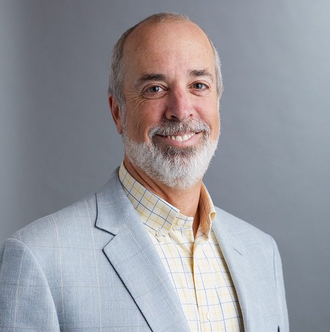 Ric Edelman, founder of the $337 billion asset management firm, smiles in a professional portrait wearing a light gray blazer over a checkered shirt, accompanying his bold prediction that Bitcoin will surge to $500,000 by 2030.