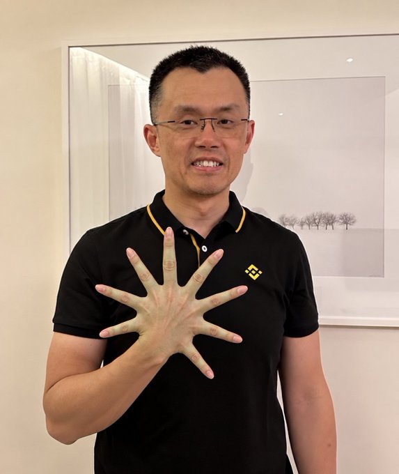 A man in a black polo shirt holding up his hand to show his palm, standing in front of a framed picture.