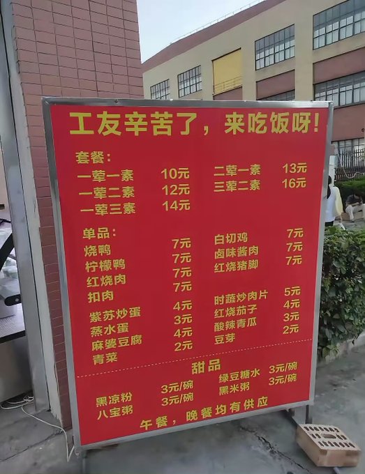 A red Chinese menu board outside displays meal sets, individual items, and desserts with prices in yuan. The header reads '工友辛苦了，来吃饭呀！' and lists options like '一荤一素 10元' (one meat one vegetable 10 yuan), with a note that lunch and dinner are both served.