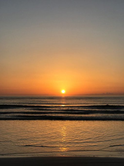 A serene sunset scene over the ocean, with the sun low on the horizon casting a golden reflection across gentle waves.