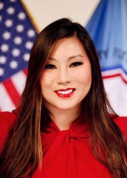 A young woman with long dark hair, wearing a red top, smiles at the camera in what appears to be an official portrait setting, with an American flag and another flag visible in the background. The image likely represents a regulatory official or spokesperson commenting on the SEC and CFTC's collaborative efforts toward establishing digital asset regulatory frameworks, as discussed in the accompanying news post.