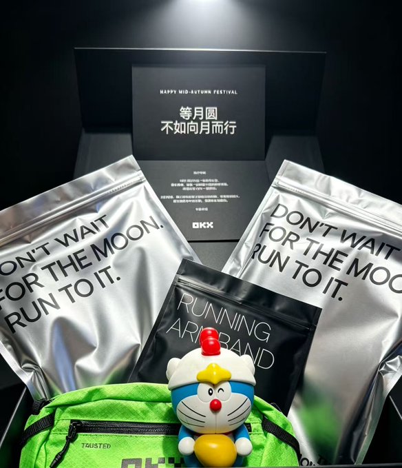 The image shows OKX's VIP Night Run Limited Edition Gift Box featuring silver pouches printed with "DON'T WAIT FOR THE MOON, RUN TO IT," a black packet labeled "RUNNING AROUND," a green "TWISTED" waist pack, and a Doraemon figurine, all displayed in front of a card reading "HAPPY MID-AUTUMN FESTIVAL" with Chinese text "等月圓 不如向月而行" (Rather than waiting for the full moon, run toward it)—a Mid-Autumn themed gift that ties into OKX's appreciation event for major clients mentioned in the post.