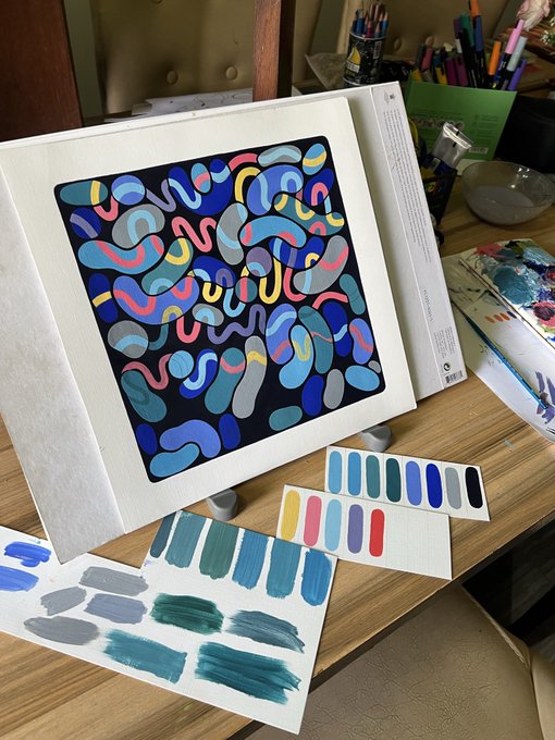 An abstract painting featuring colorful curved shapes in blues, yellows, and pinks on a black background, displayed on an easel alongside color swatches and art supplies.