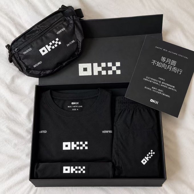 A black 'OKX' branded merchandise gift box containing a t-shirt, pants, and waist bag, accompanied by a card with Chinese text wishing 'Happy Mid-Autumn Festival'.