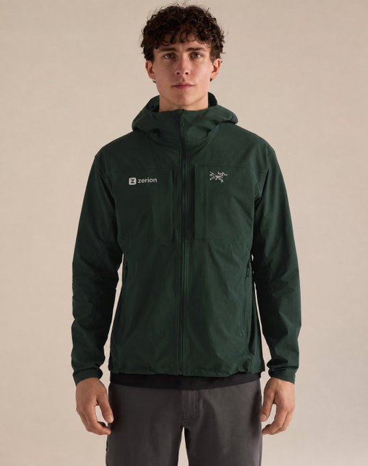 A young man with curly brown hair modeling a dark green Arc'teryx 'zerion' hooded jacket against a neutral background.