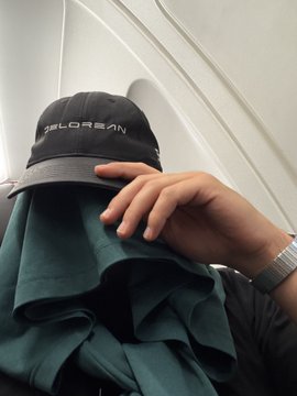 A close-up of a hand holding up a dark green cap with the word 'JAGUAR' embroidered in white lettering. The person is wearing a matching dark green top and a silver wristwatch.