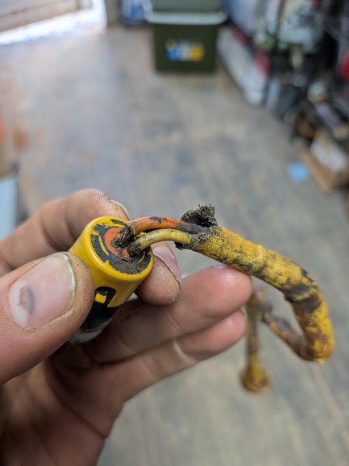 A dirt-caked hand holds a broken yellow drawcord, with frayed ends revealing the inner cord, while a partially visible "U" logo is printed on the fabric. The image humorously supports the post "Pretty sure that's not good" by showing a clearly damaged piece of outdoor gear.