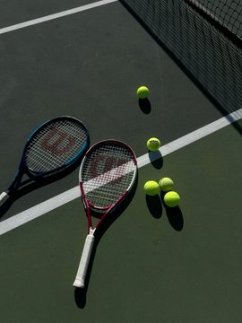 Two tennis rackets and several yellow tennis balls rest on a green court near a net, visually reinforcing the post's highlight of a Polymarket trader who earned the bulk of their profits betting on tennis underdogs. The image ties directly to the text's mention of tennis as the source of nearly all the trader's $84,094 in profit.