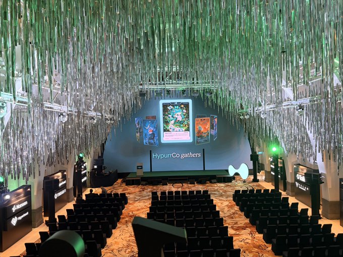 An event hall decorated with hanging green and white streamers and illuminated displays for 'HyperCo gathers', showing Pokémon-themed cards and various sponsor logos including Mastercard and HyperCo.