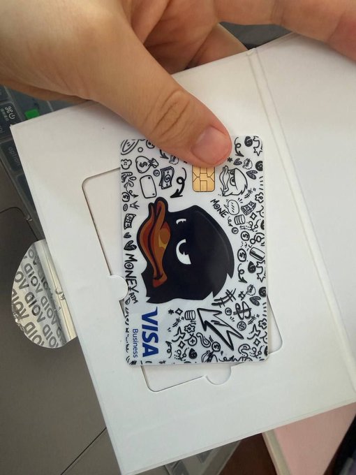 A hand holding a MonKey VISA Business debit card featuring a black cartoon monkey design with a bite mark, surrounded by doodle patterns.