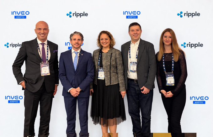Five conference attendees stand in front of a step-and-repeat backdrop featuring “INVEO CRYPTO” and “ripple” logos.