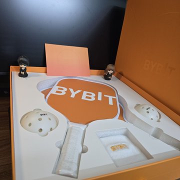 A Bybit-branded gift set is displayed, featuring two small figurines, golden tokens engraved with "2023," and the "BYBIT" logo printed on an orange balloon-shaped centerpiece, along with the "BYBIT" name on the box. The image reflects the post's gratitude to the Bybit team for a thoughtful Mid-Autumn Festival surprise, with the golden tokens likely symbolizing prosperity and the shared celebration mentioned.
