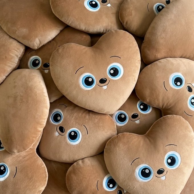 A pile of adorable brown heart-shaped plush toys with big blue eyes and small smiles are stacked together.