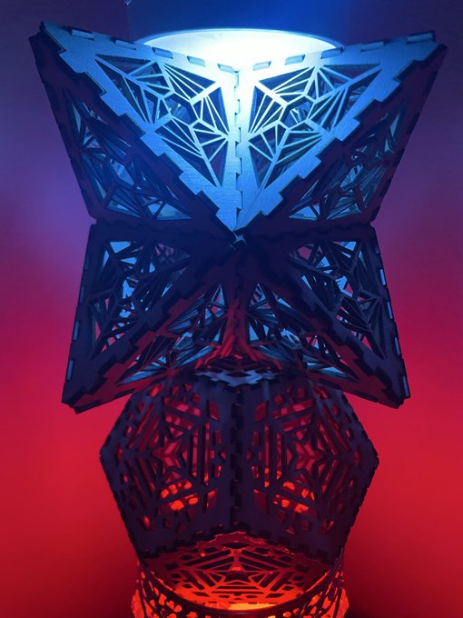 A geometric, lattice-style lamp is illuminated with blue light at the top and red light at the bottom against a gradient background.