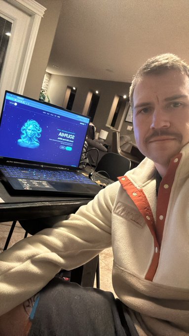 A man with a mustache wearing a fleece pullover sits beside a laptop displaying the 'AIRNODE' website.
