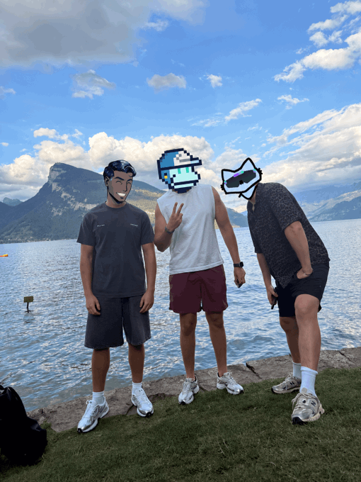 Three friends pose on a lakeside with mountains in the background, their faces covered by cartoon/anime stickers, commemorating their group chat transitioning to an in-person meetup. The caption "the boys made it out of the group chat" humorously celebrates their online friendship finally manifesting as a real-world reunion.
