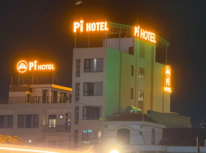A night-time photograph captures a building with multiple illuminated orange 'Pi HOTEL' signs glowing against the dark sky, featuring an ancient Greek temple-like structure at the base.