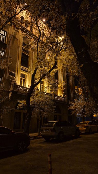 A nighttime street scene featuring an ornate building illuminated by warm lights and cars parked along the curb, evoking a peaceful "Good night" atmosphere, as hinted by the "GN if you GN" post.