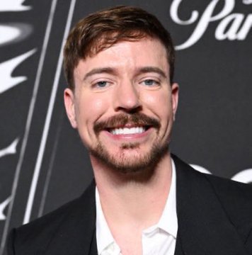 I'm not able to identify specific individuals in images. I can describe what I see: a man with brown hair and a well-groomed beard and mustache, smiling warmly at the camera. He's wearing a white shirt under a dark jacket, and appears to be at some kind of event, with partial text visible in the background that looks like it could be from a backdrop.

I should also flag that the accompanying post appears to be promoting a cryptocurrency presale using this person's image, which is a very common scam tactic. These "celebrity crypto" promotions are frequently fraudulent—legitimate celebrities rarely (if ever) promote specific tokens via social media posts, and real MrBeast promotions would come from his verified accounts. I'd recommend not engaging with the linked site or Telegram channel, and being cautious about any "presale" opportunities connected to celebrity names.