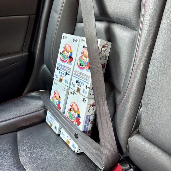 Several white product boxes labeled "CHOCO TREAT DOKIDOKI" with cartoon characters stacked in a car passenger seat and secured with a seatbelt.