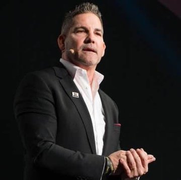 Photo of a man in a dark suit with an earpiece microphone speaking on stage, likely giving a presentation or speech.