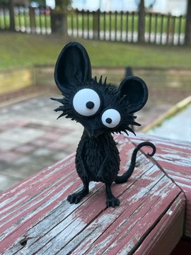 A small black handmade figurine with large round eyes, pointed ears, and spiky fur stands on a weathered red wooden bench.