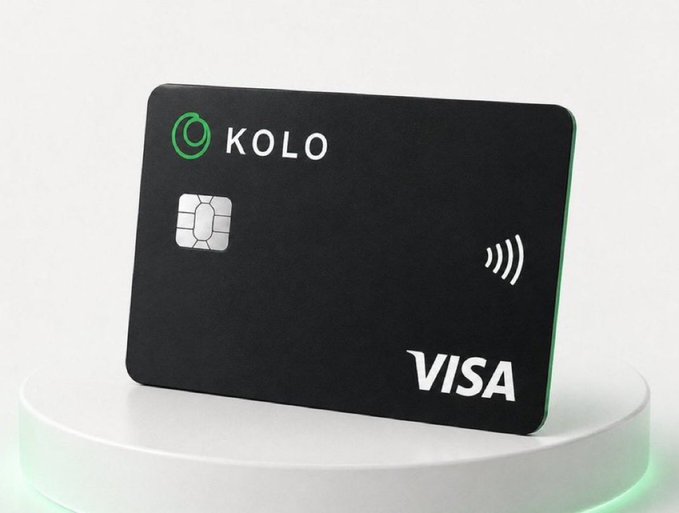 The image features a black credit card from KOLO, which has a green logo on its back. The credit card is placed on top of a white surface, possibly a table or countertop. The background of the image is blurred, drawing attention to the credit card and making it the main focus of the scene.