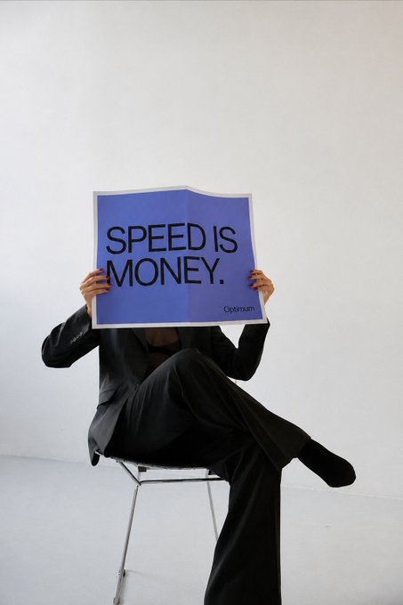 A person in a black suit sits on a chair holding up a blue sign that reads "SPEED IS MONEY." with "Optimum" in the corner.