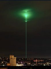 A nighttime cityscape featuring a strange, bright green vertical beam of light or phenomenon shining down from the clouds.