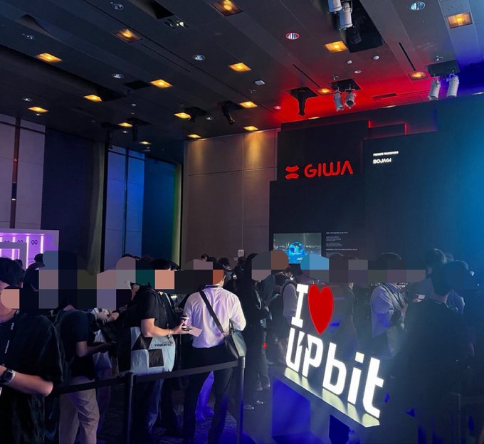 A crowded event space at KBW2026 features attendees gathered in front of illuminated booths, including a prominent "I ❤️ upbit" sign and logos for GIWA and BORA, with a screen displaying BORA above the crowd. The scene captures the busy atmosphere of Day 1 of the conference, where Upbit is showcasing its presence ahead of additional meetings the following day.