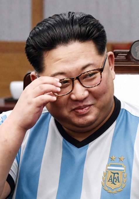 Kim Jong Un is pictured wearing an Argentina national football team jersey with the 'AFA' crest visible on the chest, adjusting his glasses.