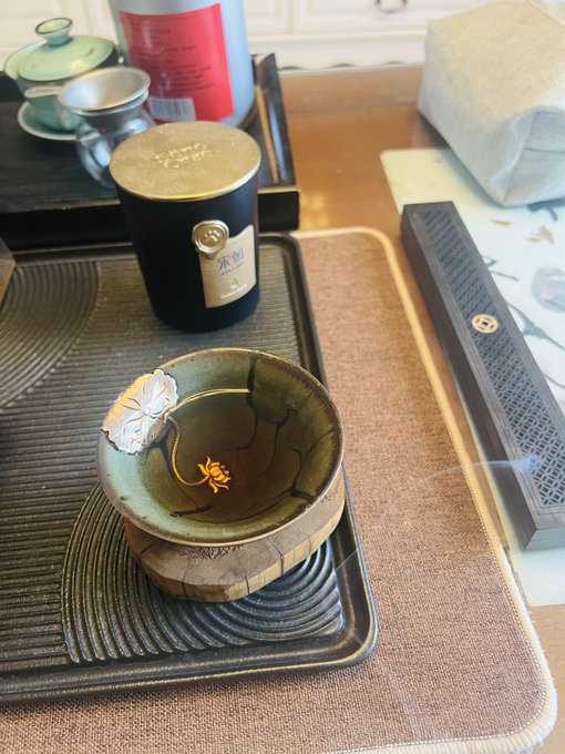 A traditional Chinese tea set featuring a dark ceramic tea canister labeled "东则" (Dong Ze) with a small matching bowl containing tea and a decorative leaf, all arranged on a wooden tray. The image evokes a serene weekend morning tea ritual, complementing the post's relaxed tone about handling an expired car insurance quote from Ping An and taking the bus instead.