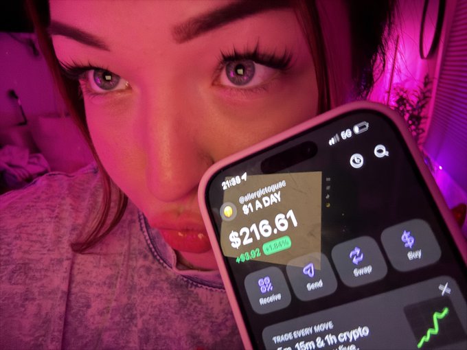 A close-up selfie of a person with purple-lit eyes holding a phone displaying a crypto portfolio showing '$216.61' with a green '+8.92' gain and '1.64%', with 'Gallergetique' visible on the screen.