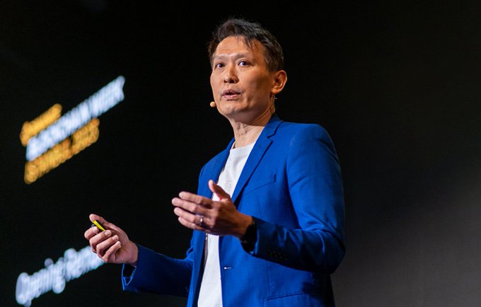 A man wearing a blue suit is speaking at a stage with a screen behind him, which has #crypto and $5.6B written on it and also shows other cryptocurrencies like Bitcoin and Ethereum being exchanged for Ether. The event has attracted crypto enthusiasts and investors looking to invest in the cryptocurrency market or learn more about it.