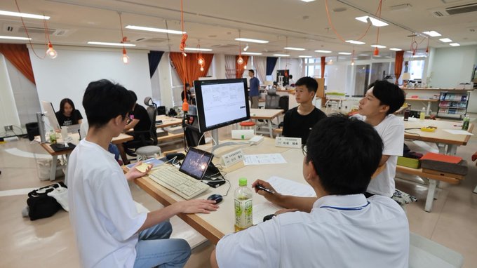 High school students in Nagasaki collaborate around a monitor displaying code in a classroom, learning about vibe coding and JPYC as part of their course.