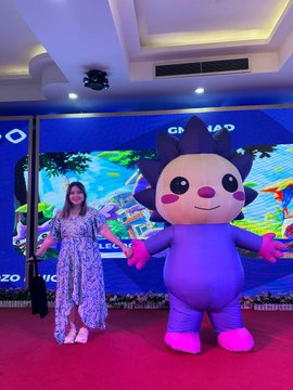 A woman in a floral dress stands next to a large purple mascot character at an OPPO event.