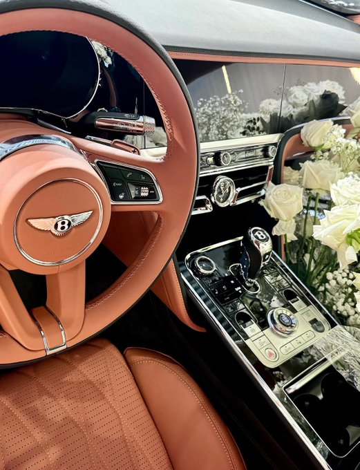 Interior of a luxury Bentley with peach/orange leather upholstery and a bouquet of white roses on the dashboard.
