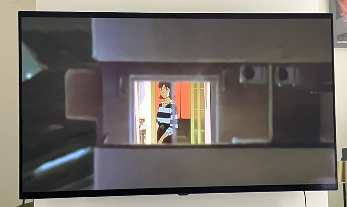 A photo of a wall-mounted television displaying an animated scene featuring a character with dark hair and a striped shirt standing in a doorway.