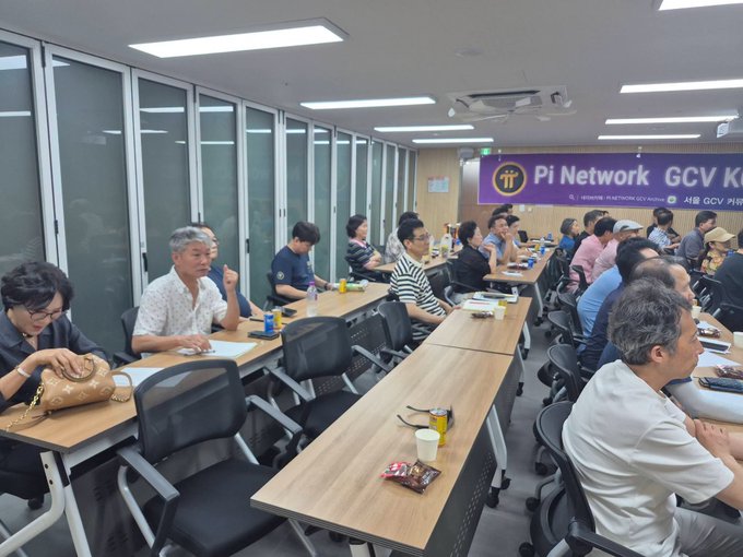 A meeting or presentation room in Korea with attendees seated at tables, featuring a purple banner that reads 'Pi Network GCV' in the background.