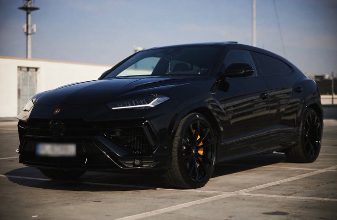 A glossy black Lamborghini Urus SUV is parked on a rooftop lot, its sleek lines and orange brake calipers standing out against the concrete surface, fitting the post's tongue-in-cheek "I just put diesel in my Lambo AMA" with the visible Lamborghini badge on the hood.