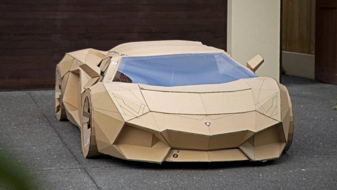 A full-size, working replica of a Lamborghini Aventador constructed entirely out of cardboard, complete with angular body panels and blue-tinted windows.