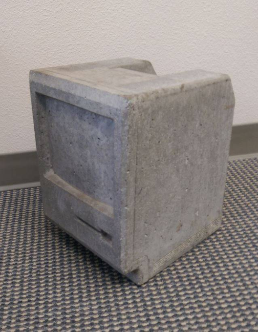 A weathered gray plastic crate or container sitting on a blue and white patterned mat against a plain wall.