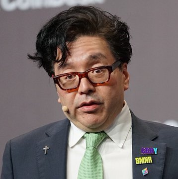 A man wearing glasses, a dark suit, and a green tie speaks at a podium with a headset microphone, displayed with a Bloomberg TV (BKNTV) watermark suggesting a live financial broadcast. The image relates to the post about $ETH ETFs experiencing $319.97 million in weekly net outflows, likely showing a commentator discussing this crypto market development.